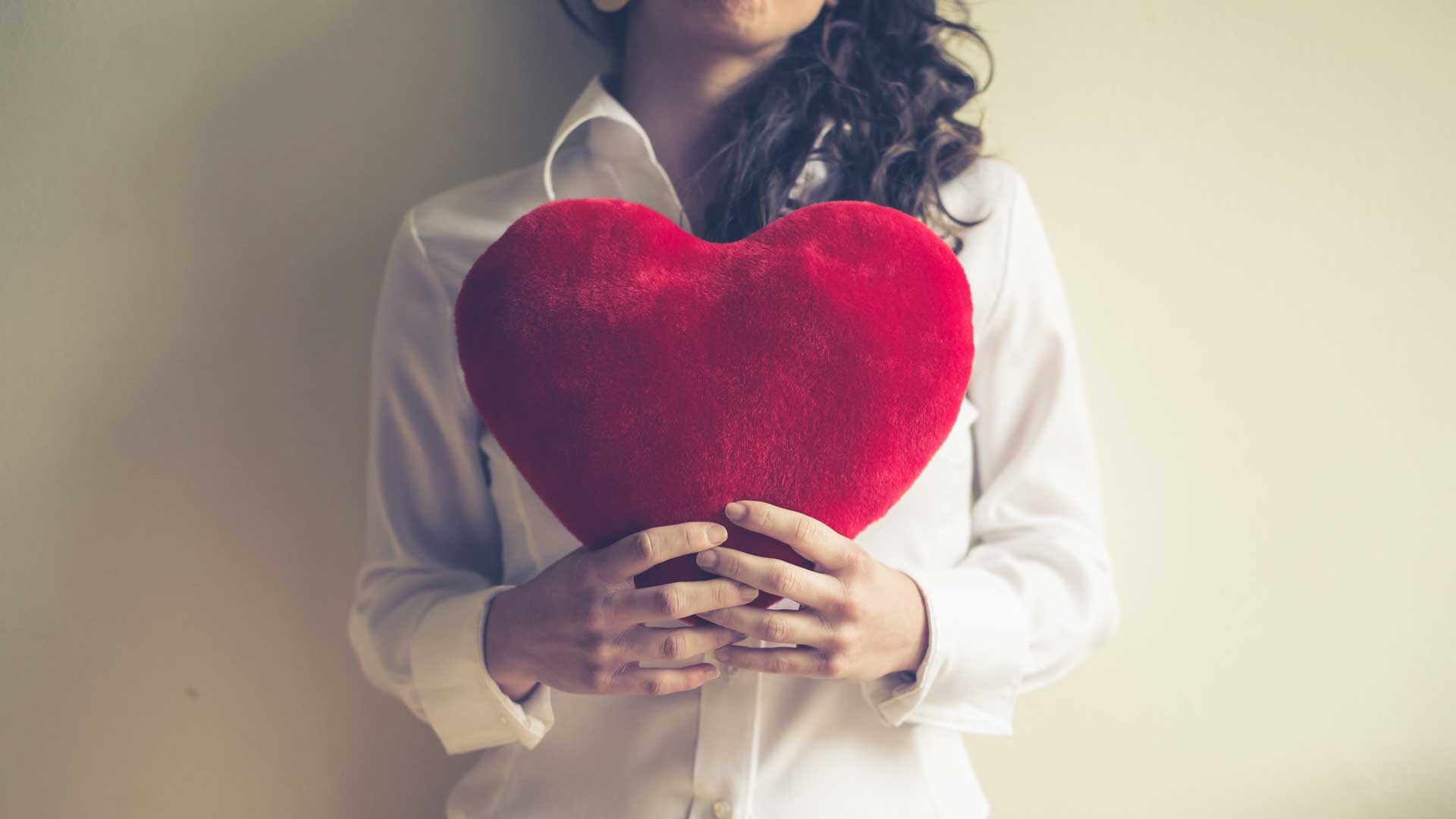 Woman holding red plush heart in front of her chest
