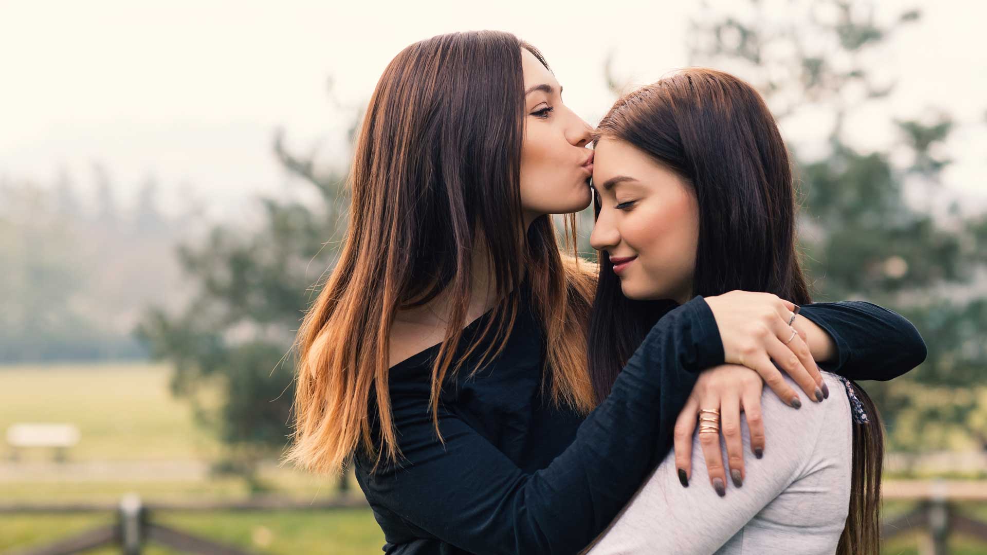 Portrait of young sisters hugging and kissing outdoors in a park