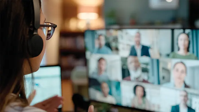 A woman sits in front of a computer screen with multiple participants showing on the screen.
