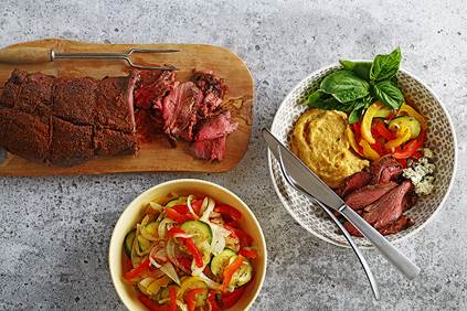 Balsamic beef tenderloin on a cutting board with vegetables and polenta served in dishes