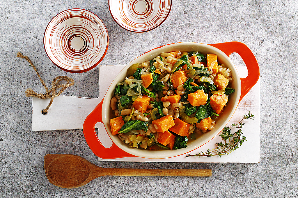 Bean, sweet potato and garlic stew in a red serving dish with bowls alongside.