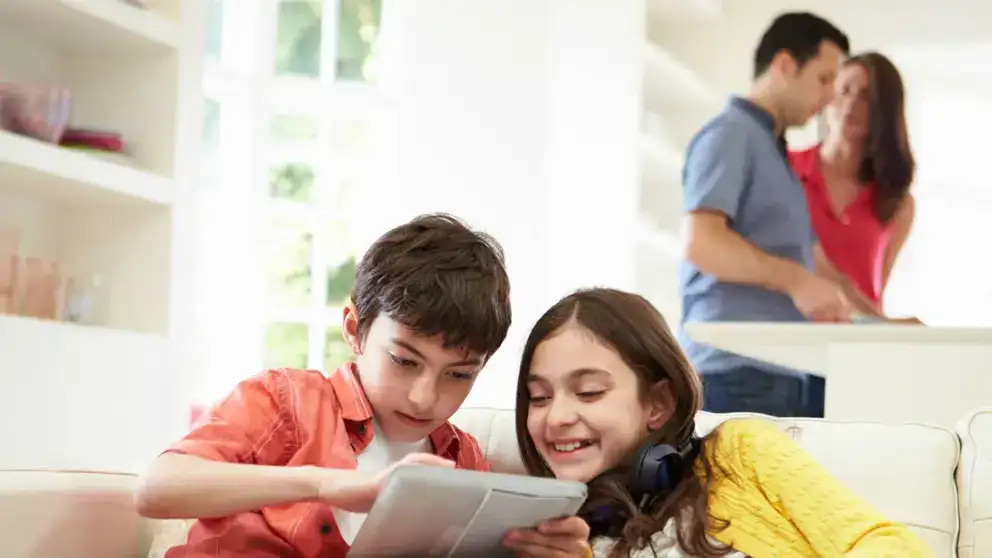 brother and sister playing on tablet while parents prepare dinner