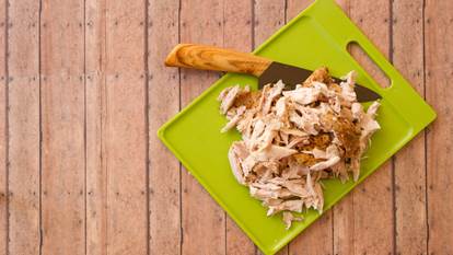 Shredded rotisserie chicken on a green plastic cutting board and carving knife