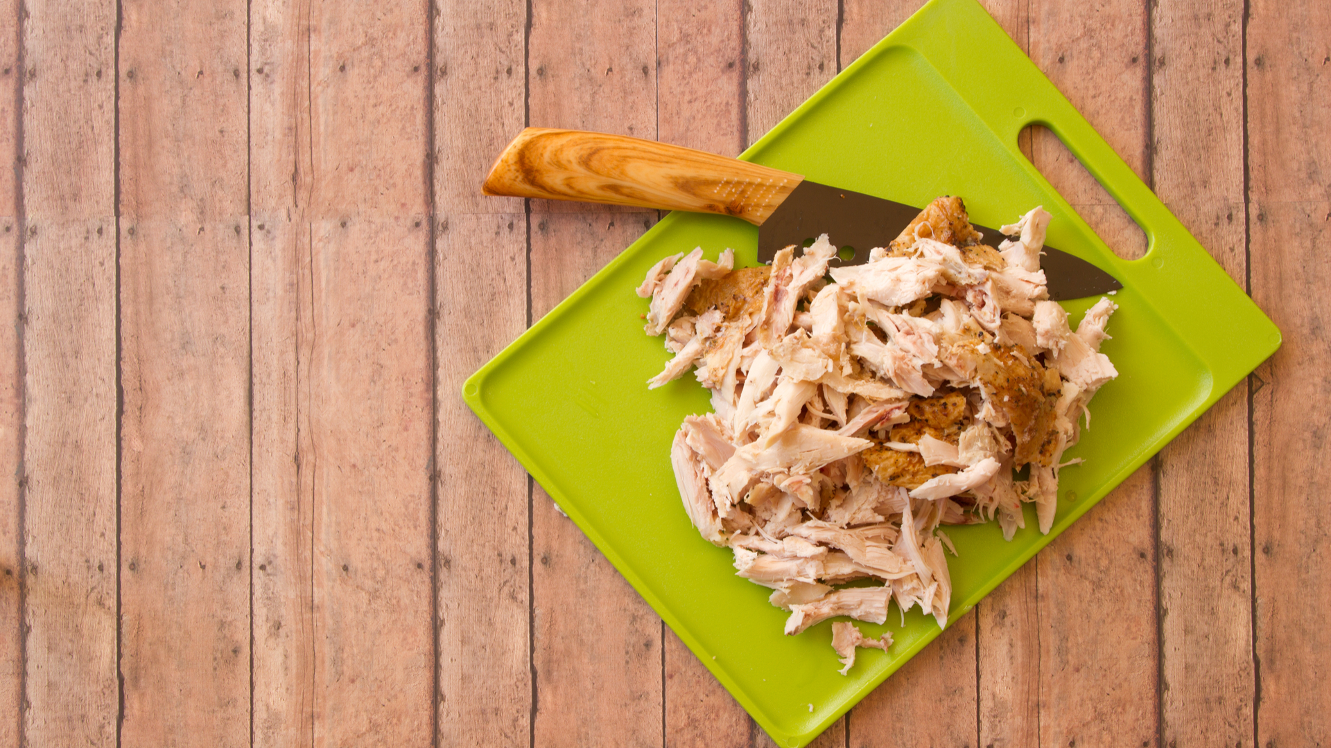 Shredded rotisserie chicken on a green plastic cutting board and carving knife