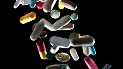 Pills of all colours, shapes and sizes falling in front of a black background