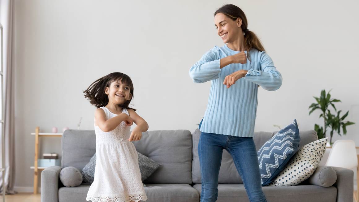 A mother and her daughter dance in their living room 