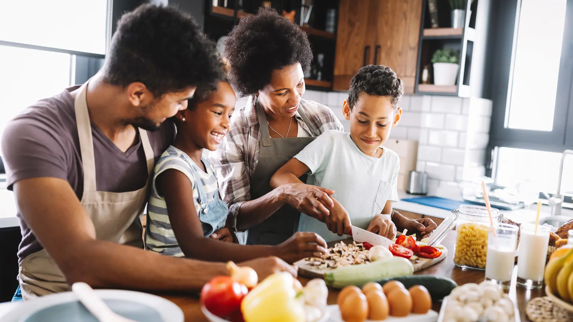 Two adults and two children prepare food together in a kitchen.