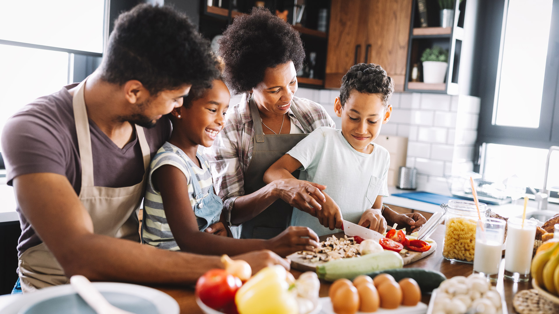 Two adults and two children prepare food together in a kitchen.