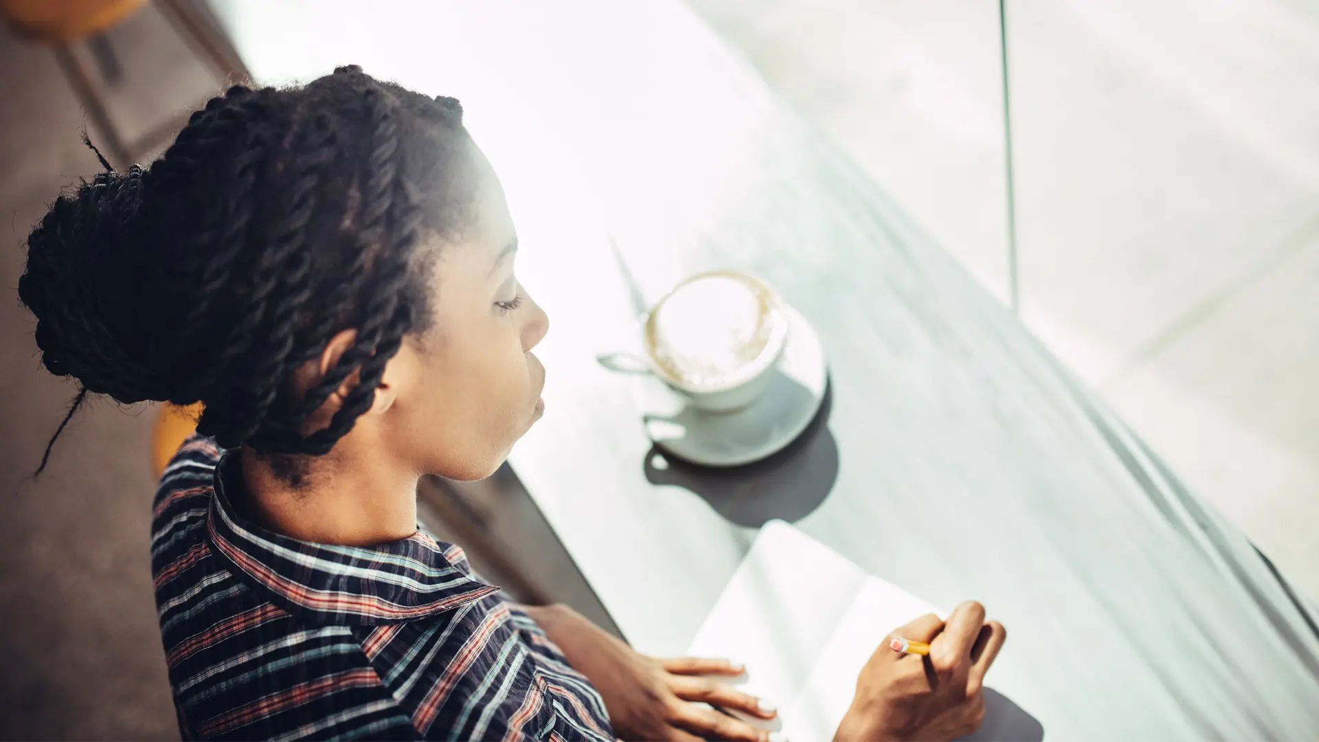A woman sitting drinking coffee and writing in her journal