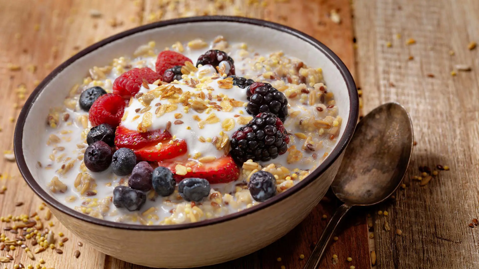 A bowl of oatmeal and berries next to a spoon.
