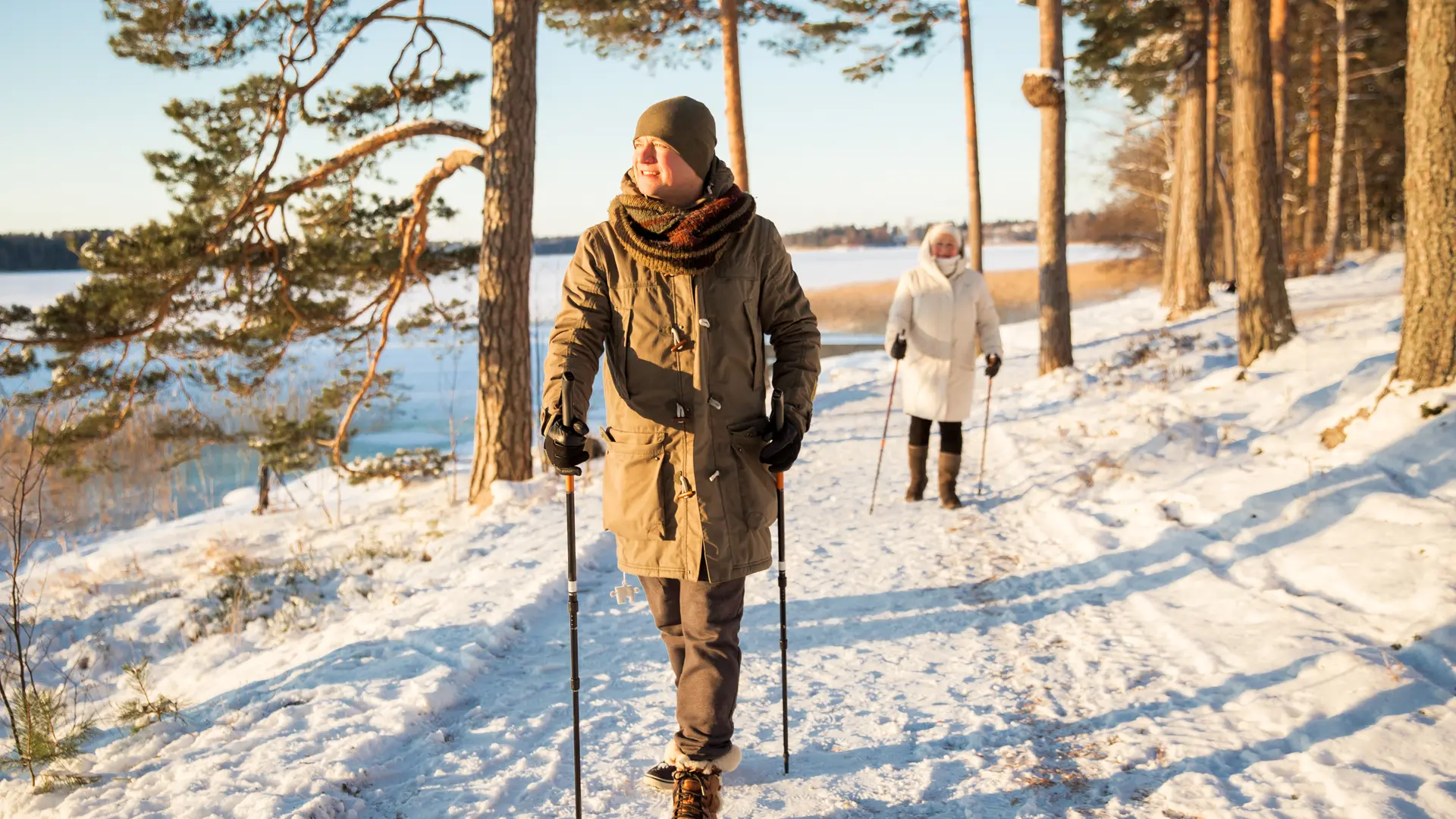 A senior couple walking on a snow covered trail by a lake.