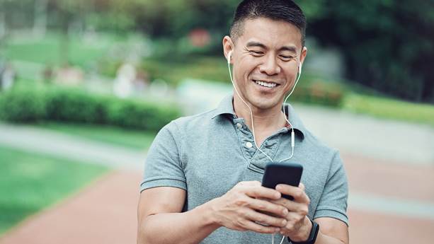 A smiling man types on his cellphone in the park.