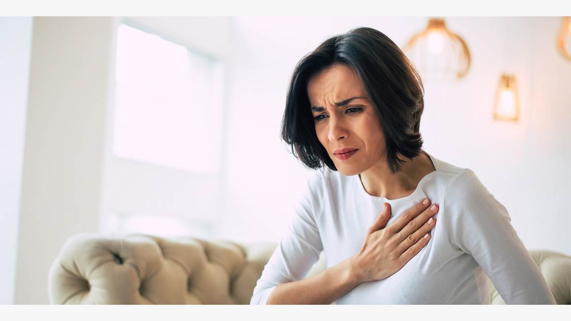 A woman holds her hand to her chest while experiencing discomfort