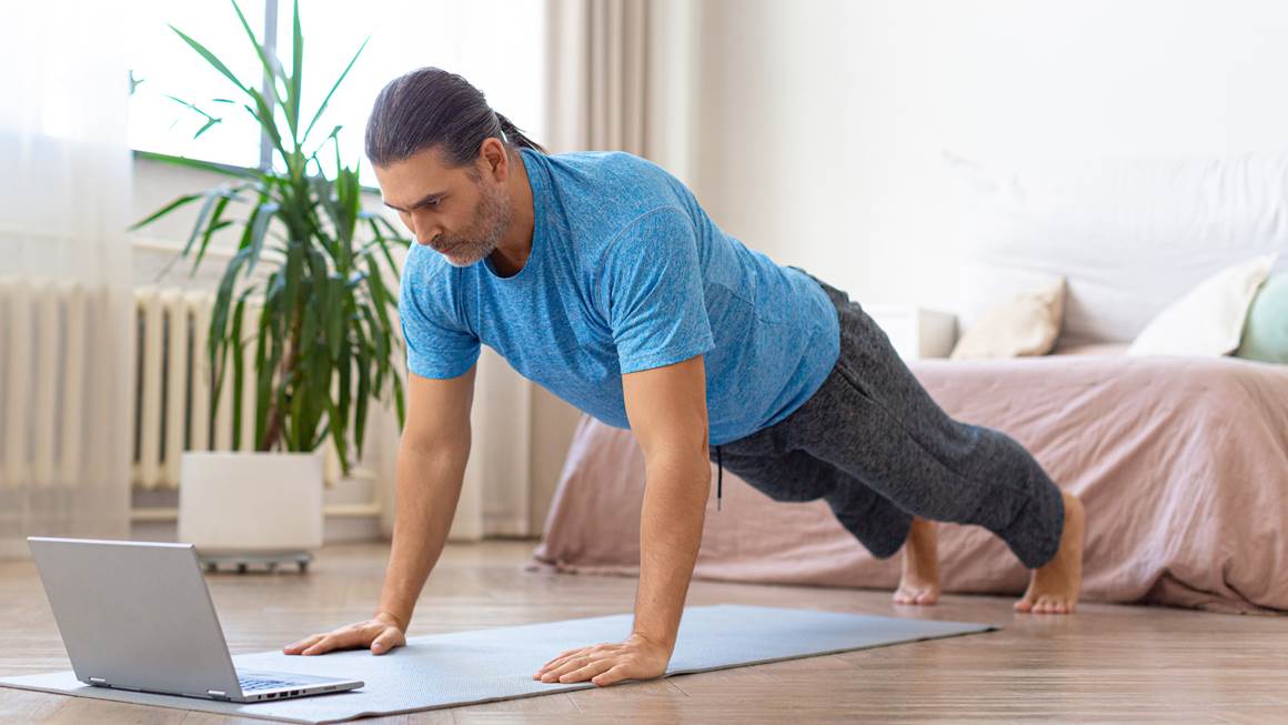 A man doing push-ups at home while watching a laptop
