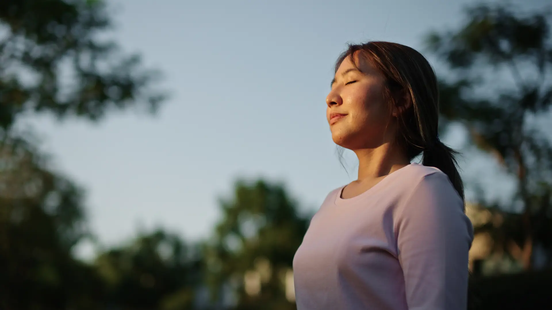 A person standing outdoors with their eyes closed.