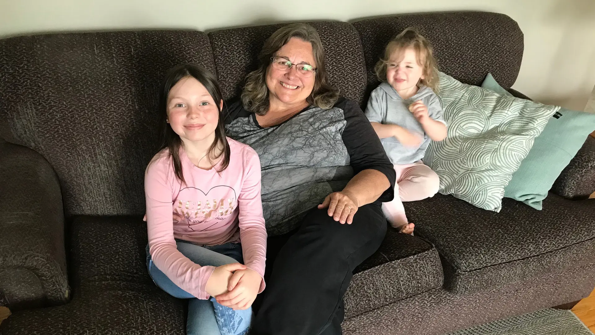 Emily Coyle sits on a couch with her grandmother, Wendy Grohs, and sister, Charlotte.