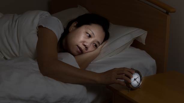 Woman with insomnia touching alarm clock