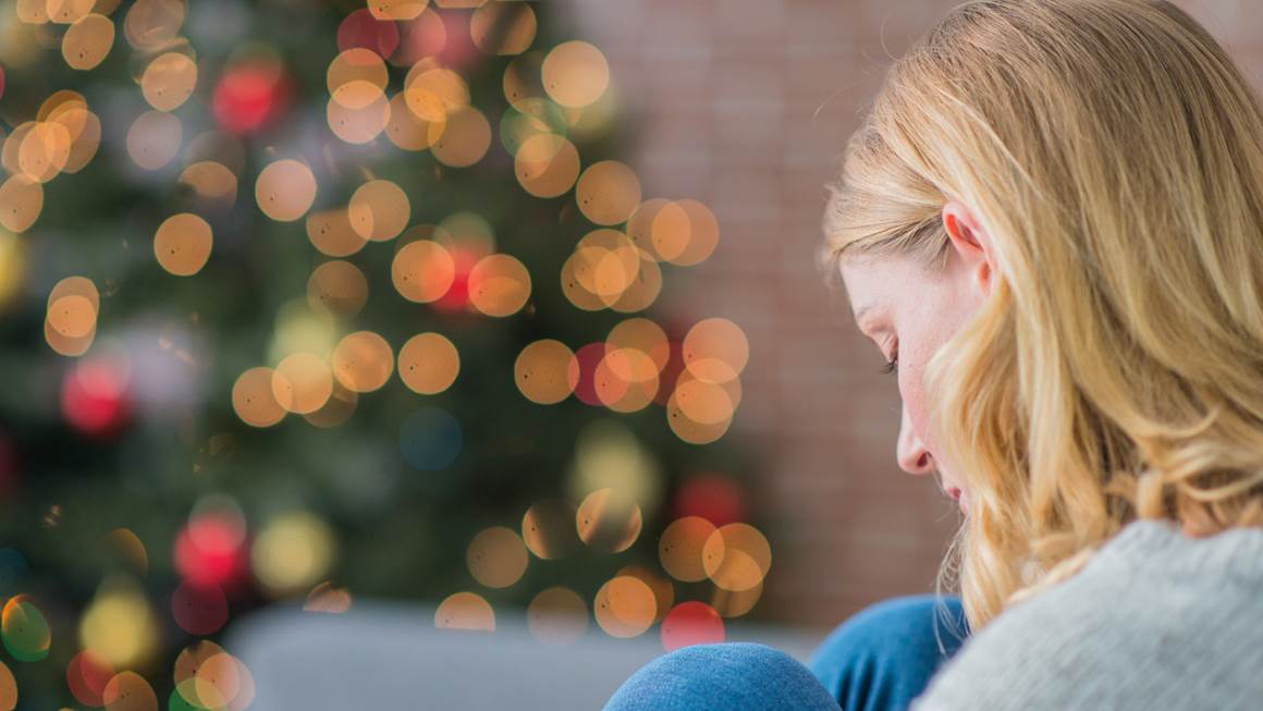 Woman sitting in front of a christmas tree looking sad