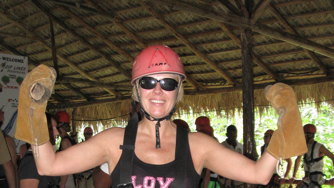 Beth Luhowy smiles wearing a pink helmet and a zipline harness.