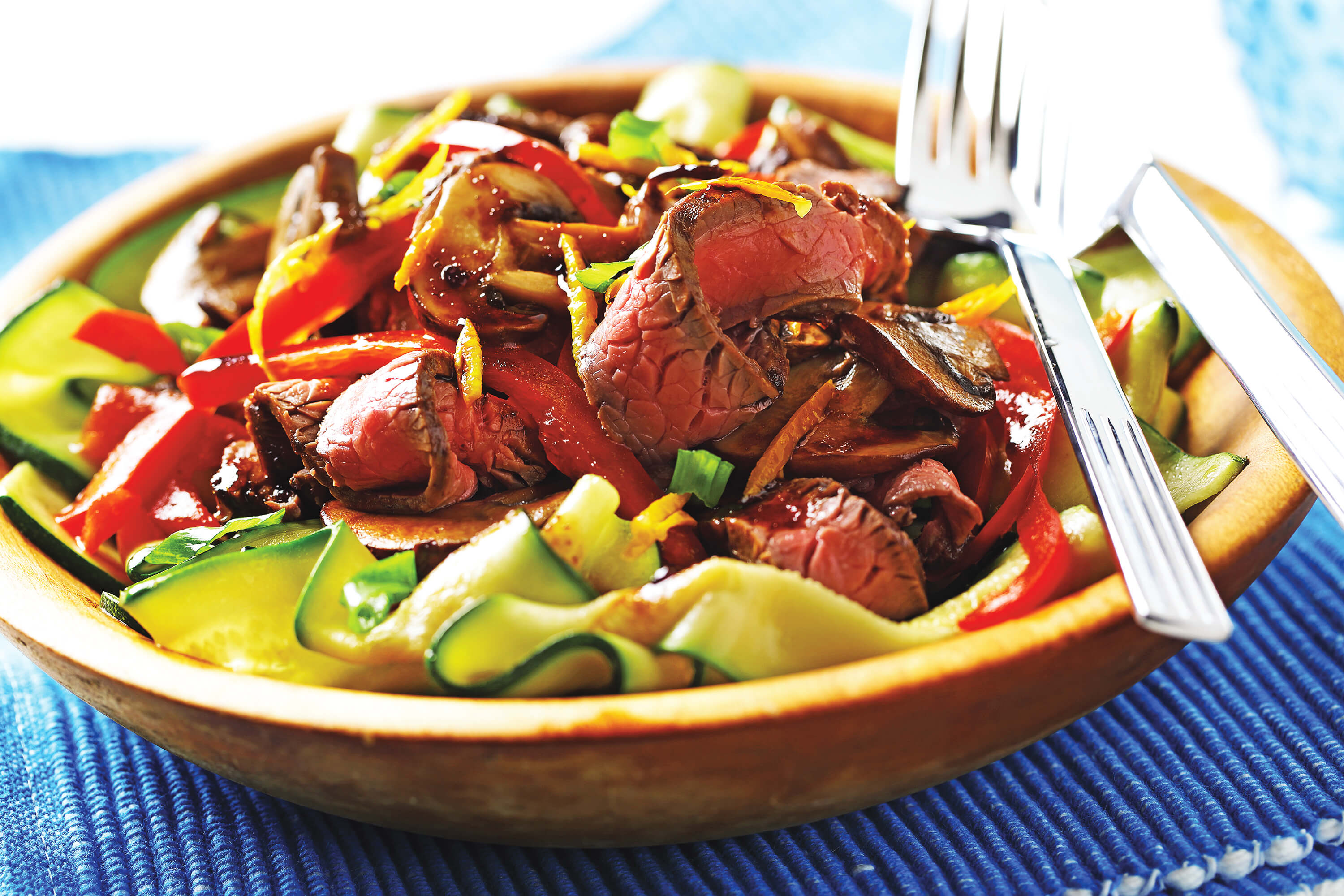 Slices of beef, zucchini ribbons and red peppers in a bowl