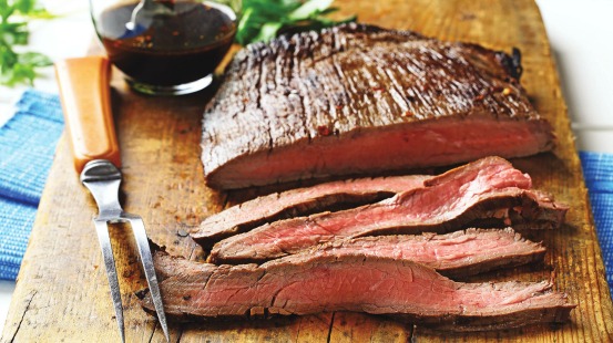 Sliced flank steak on wooden cutting board 