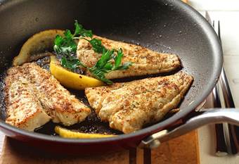 Three pieces of cooked fish in pan with lemon and herbs 