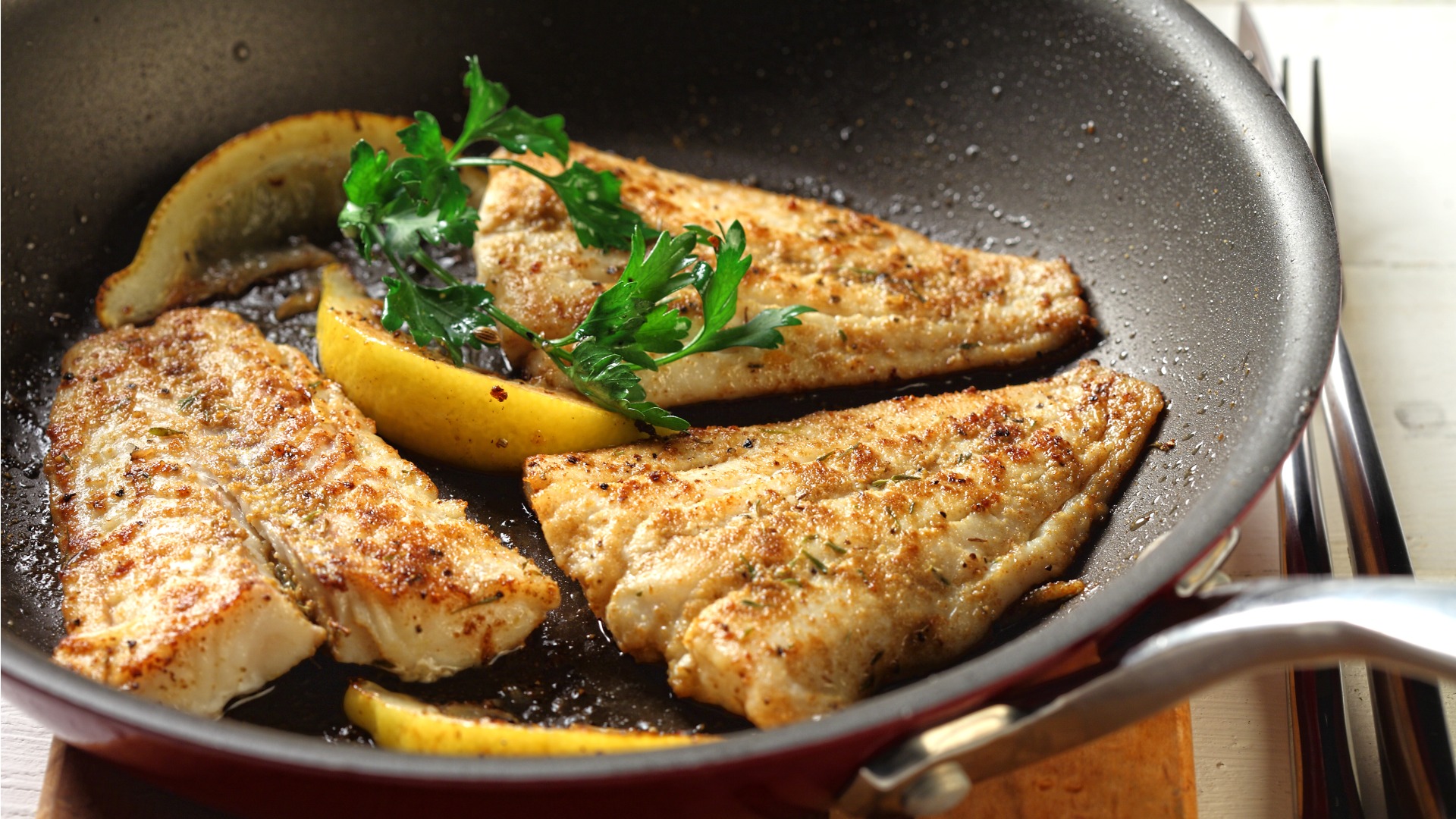 Three pieces of cooked fish in pan with lemon and herbs