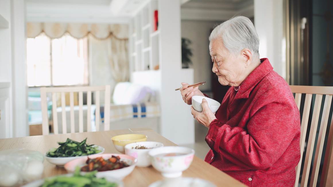 Elderly man eating from bowl with chopsticks 
