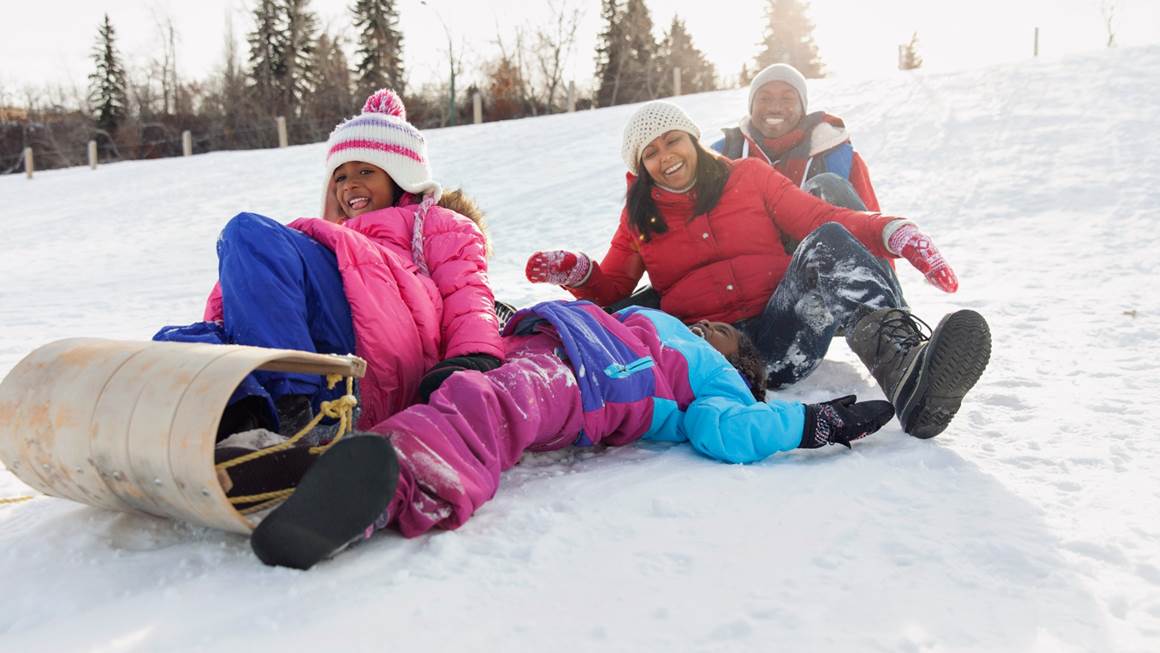 Family laughing as they toboggan down a snow-covered hill