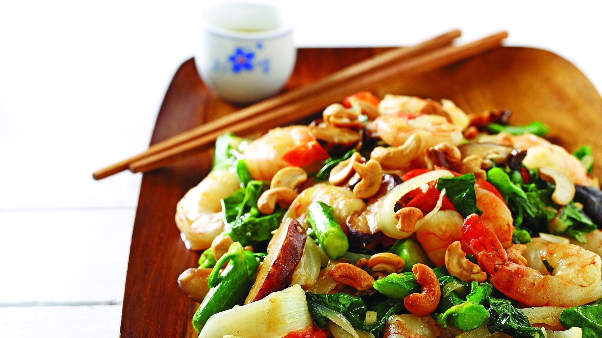 Shimp, bok choy, red peppers, cashews on wooden board with chopsticks