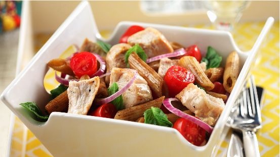 Bistro chicken pasta  salad in a square white bowl with a fork on a yellow tablecloth