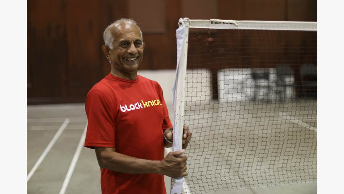 Jerry Alfonso wears a read T-shirt as he stands beside a badminton net in a gymnasium.