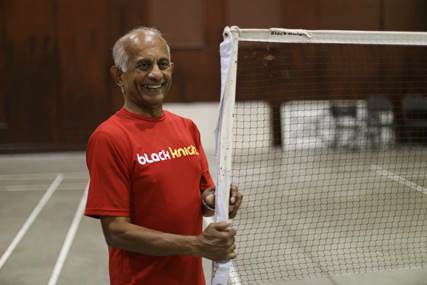 Jerry Alfonso wears a read T-shirt as he stands beside a badminton net in a gymnasium.