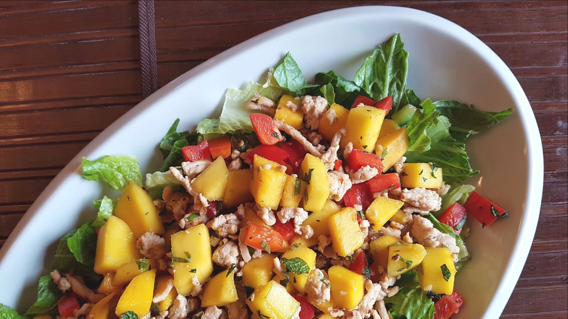 Diced mango, chicken, lettuce, red peppers on white plate 