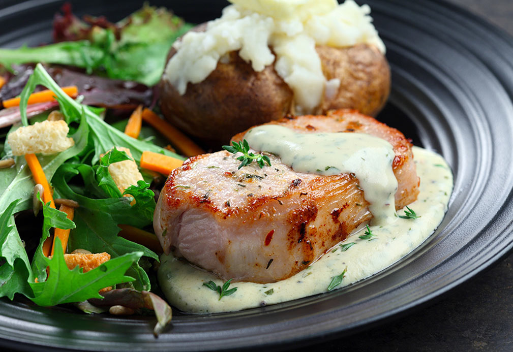 Plate with side salad, baked potato and porkchop drizzled with mustard sauce