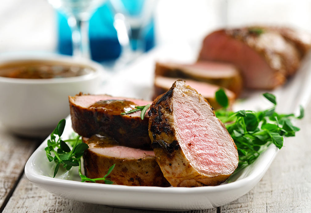 Sliced pork tenderloin with maple sauce on plate with greens