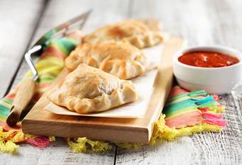 Three mini calzones on wooden cutting board with bowl of marinara dipping sauce.