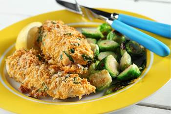 Plate with two pieces of battered halibut fillets, cooked brussel sprouts and sliced lemon wedge