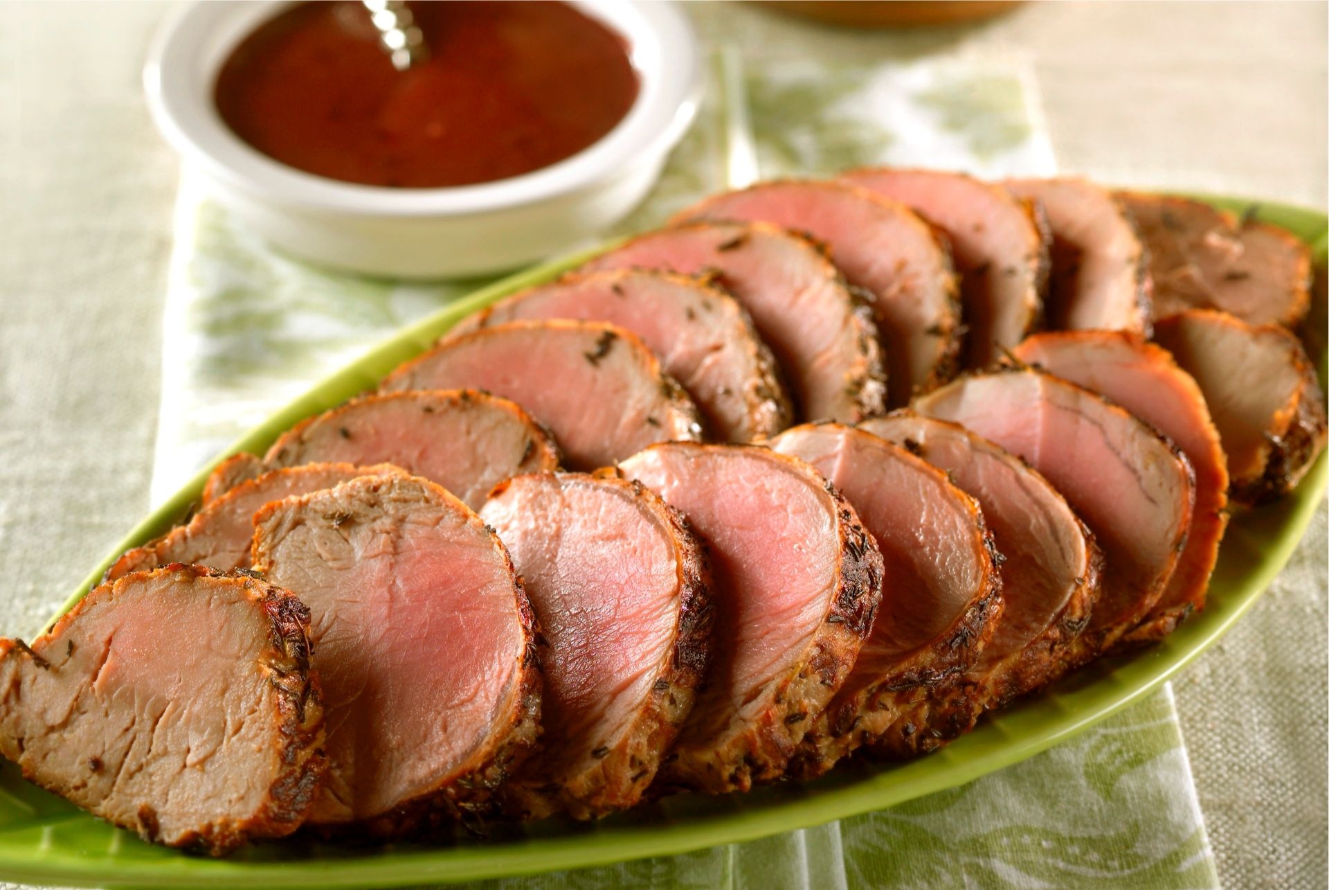 Platter of sliced pork tenderloin with small dish of raspberry mustard sauce in background