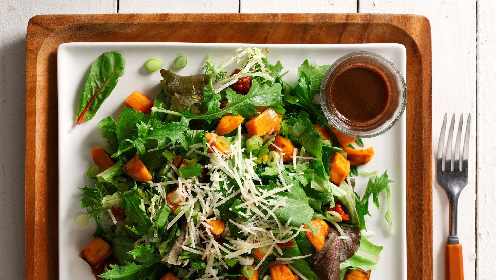 Warm sweet potato, sundried tomato and arugula salad on a white square plate.