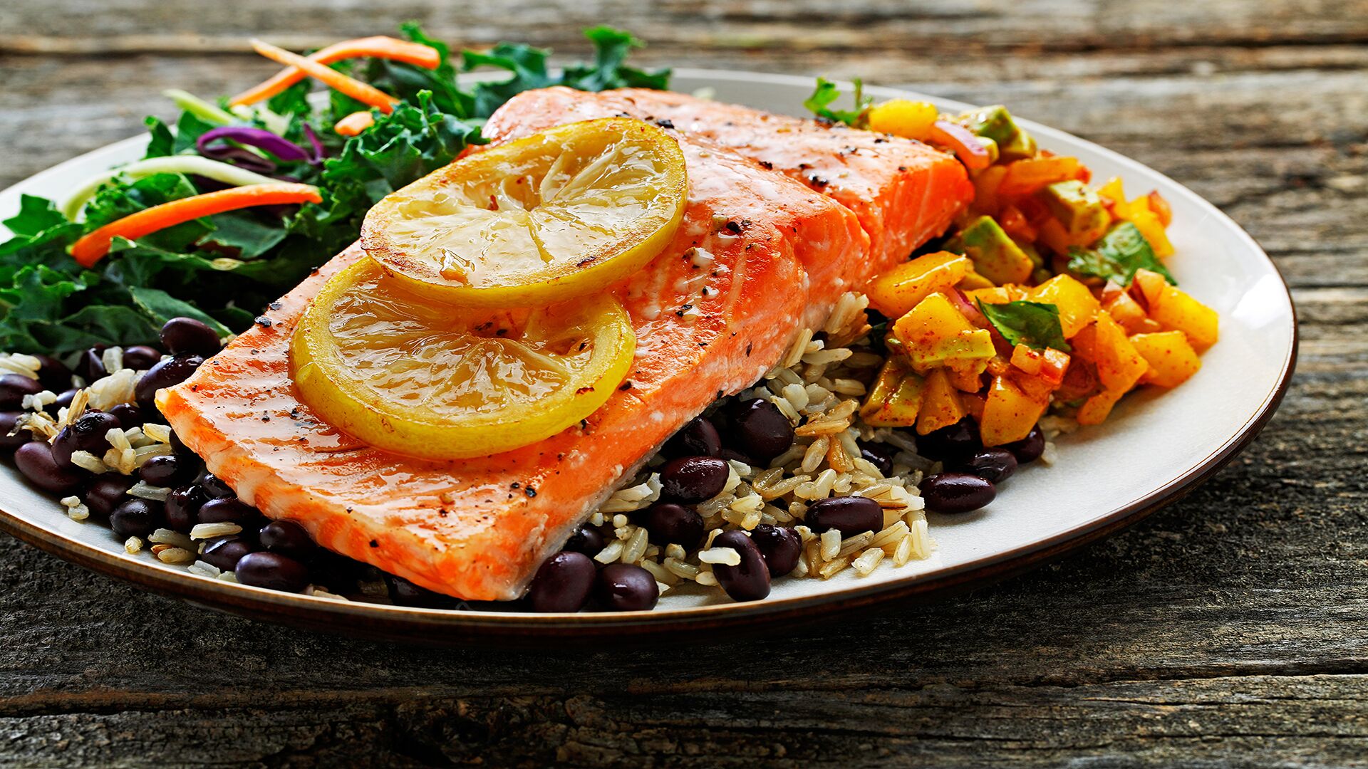 Plate of roasted trout, mango salsa, rice, black beans and green salad