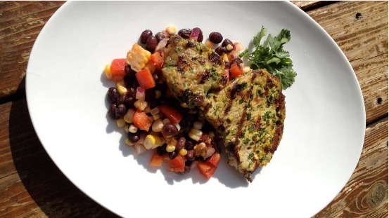 Pork with black bean salad on a large white plate on a wooden table