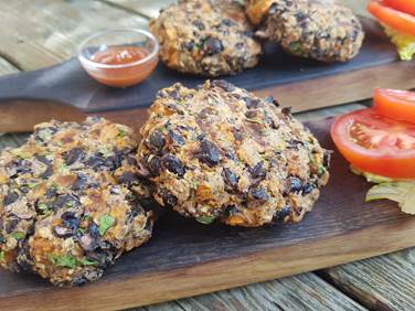 Sweet potato and black bean burger patties on wooden board with tomato slices