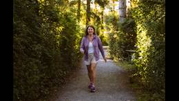 Tracy Bawtinheimer wears a purple jacket and shorts as she walks in the woods.