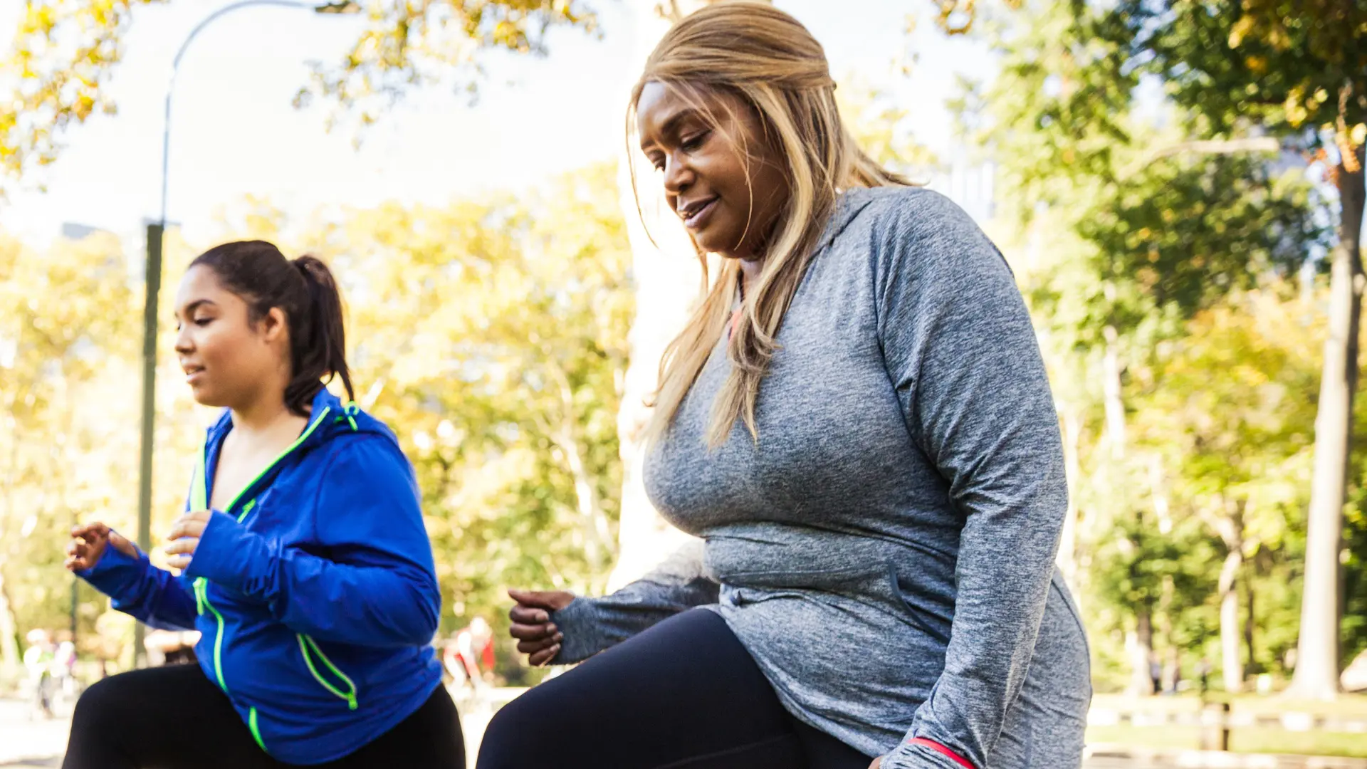 Two women doing lunges on park bench outdoors