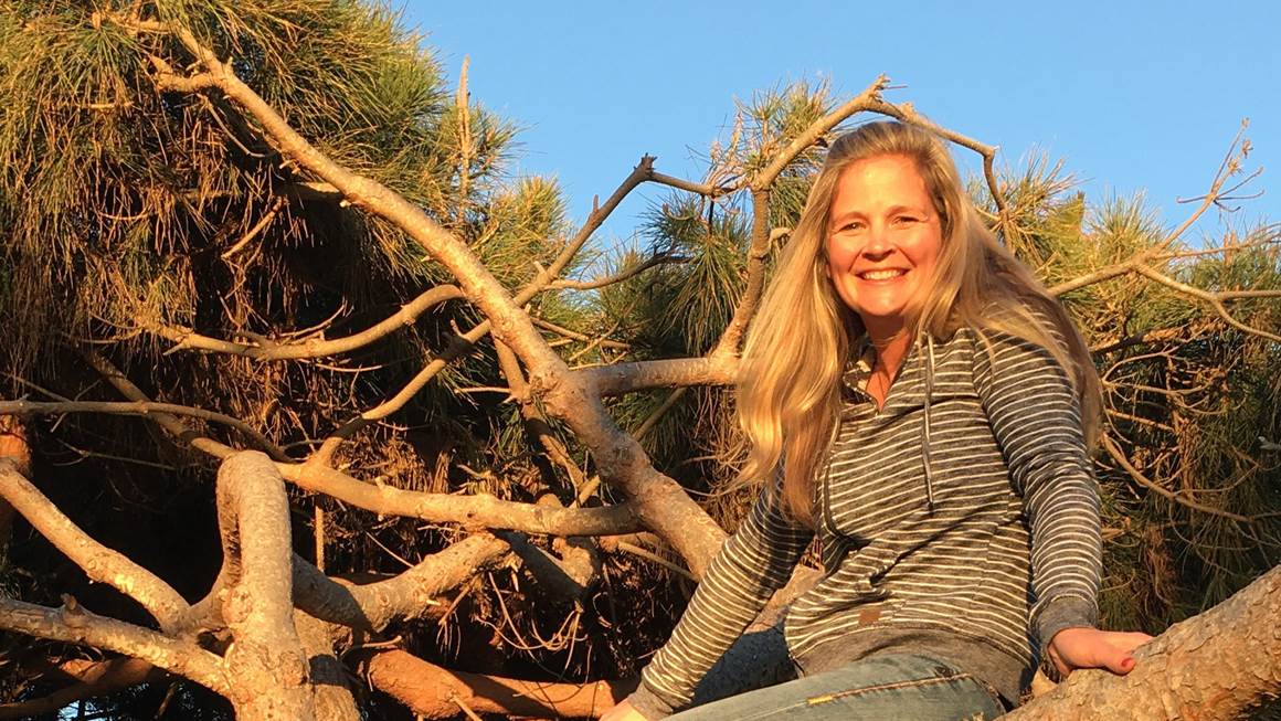 Wendy Swain smiles at the camera while posed on a tree