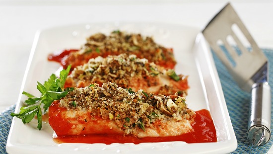 Cooked fish topped with herbs on white plate with red sauce