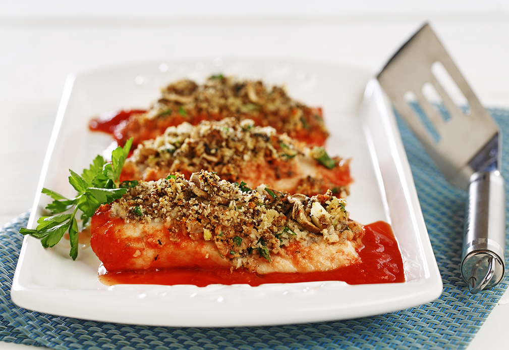 Cooked fish topped with herbs on white plate with red sauce