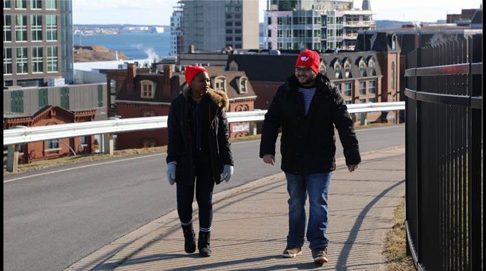 Two volunteers wearing red toques walk on a city street.