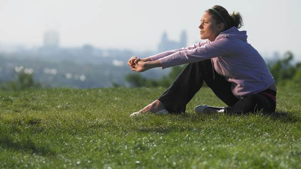 Young woman sitting on grass in sport clothes cityscape in background v2